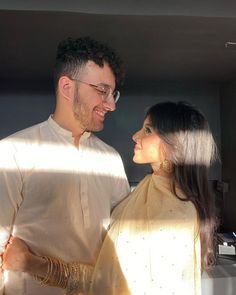 a man and woman standing next to each other in front of a window with the sun shining on them