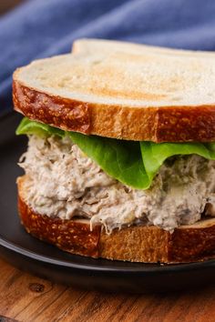 a sandwich with meat and lettuce is on a black plate next to a blue towel