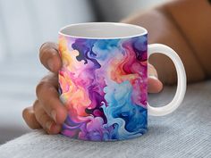 a person holding a colorful coffee mug in their left hand, with an artistic design on it