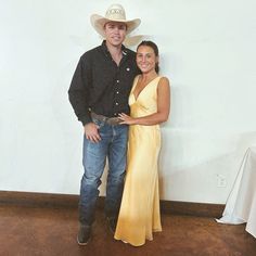 a man and woman standing next to each other in front of a wall wearing cowboy hats