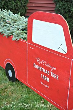 an old red truck with a christmas tree in the back is sitting on some grass