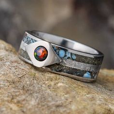 a silver ring with a red and blue stone in the center on top of a rock