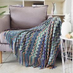 a couch with a blanket on it next to a white table and bookshelf