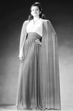 an old photo of a woman in a long dress with a cape on her head