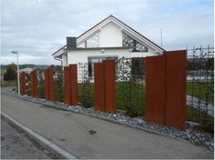 a house behind a fence that is made out of wood and metal with plants growing on it