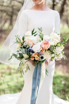 a bride holding her bouquet in front of the camera, wearing a white dress and blue sash