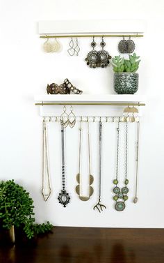 a wall mounted jewelry rack with several different necklaces and earrings on it next to a potted plant