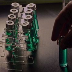 a hand is pointing at some green plastic tubes on a table with other items in the background