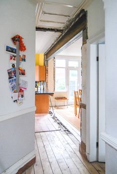 an open door leading to a kitchen and living room area with hardwood floors, white walls and exposed beams