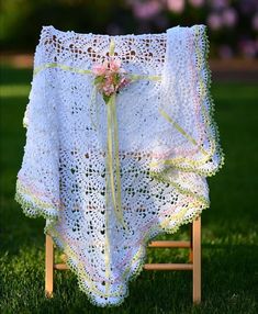 a crocheted blanket draped over a wooden chair in the grass with flowers on it