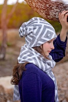 a woman wearing a gray and white scarf holding a tree branch