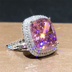 a fancy pink diamond ring sitting on top of a wooden table with diamonds around it