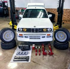 a white car parked in a garage next to some tires and wrenches on the ground