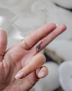 a person's hand with a tiny tattoo on the middle finger, holding up their fingers