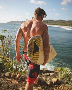 a shirtless man carrying a surfboard near the ocean