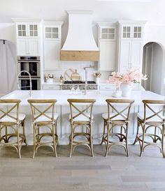 a large kitchen with white cabinets and wooden chairs in the center island, surrounded by four stools