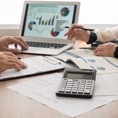 three people sitting at a table with laptops and calculator in front of them