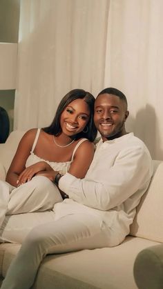 a man and woman sitting on top of a couch smiling at the camera with their arms around each other