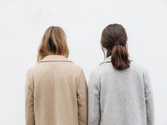 two women standing next to each other in front of a white wall and looking at the sky