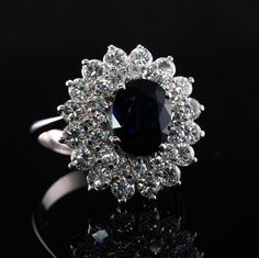 This estate ring is crafted in solid 18K White Gold (carefully tested and guaranteed). The center natural Earth mined oval cut Sapphire measures 9x7mm (2.20 carats). This gem has a deep blue color. It also has a tiny chip that cannot be seen without magnification. The center stone is surrounded with 32 round brilliant cut diamonds. 16 diamonds total 1.28 carats and smaller 16 gems total .64 carats. The grand total diamond weight is 1.92 carats of VS1 clarity and G color. Size 7 (sizable). The ri Luxury Cluster Ring With Oval Center Stone, Luxury Oval Cluster Ring With Center Stone, Luxury Oval Cluster Ring With Halo Setting, Elegant Cluster Sapphire Ring, Gia Certified, Elegant Gia Certified Cluster Sapphire Ring, Elegant Cluster Flower Ring With Halo Setting, Luxury Gemstone Flower Ring For Formal Occasions, Elegant Oval Gia Certified Cluster Ring, Luxury Oval Gemstone Flower Ring