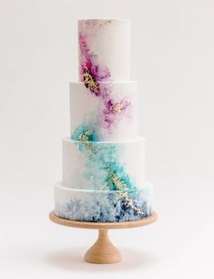 a multi - tiered cake with blue, pink and white icing on a wooden stand