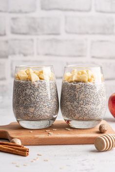 two glasses filled with chia pudding on top of a cutting board next to an apple