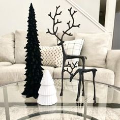 a glass table with two black trees on it and a white chair in the background