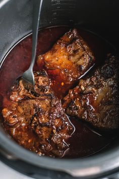 the meat is being cooked in the slow cooker with a spoon and sauce on it