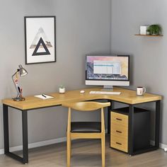 a corner desk with a computer monitor and keyboard on it in front of a gray wall