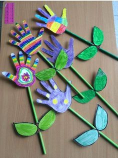 paper flowers and leaves on a table with colored crayon markers in the shape of handprints