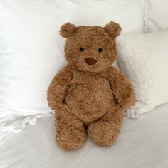 a brown teddy bear sitting on top of a bed next to white pillows and blankets