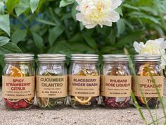 five jars filled with different types of spices and herbs sitting in front of some flowers