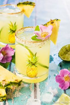 two glasses filled with pineapple margaritas and garnished with flowers on the rim