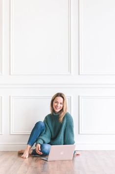 a woman is sitting on the floor with her laptop in front of her and smiling