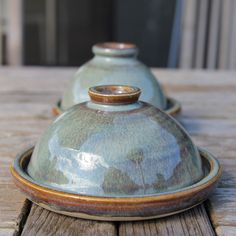 two blue pottery covered dishes sitting on top of a wooden table next to each other