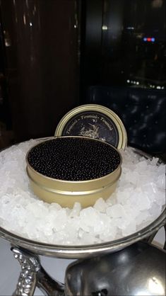 a tin with some black beads on top of it sitting on white ice in front of a window