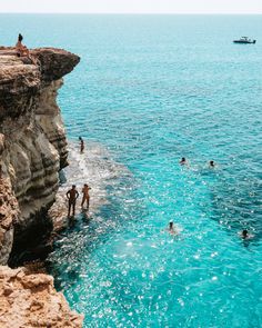 people are swimming in the ocean near some cliffs