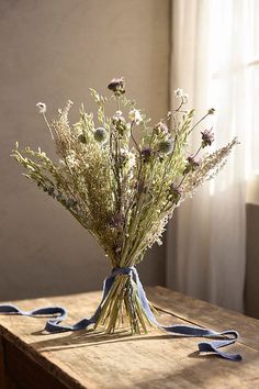 a bouquet of dried flowers sitting on top of a wooden table next to a window