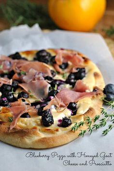 a pizza topped with blueberries and ham on top of a piece of parchment paper