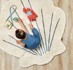 a little boy laying on top of a white rug next to a toy crab and other items