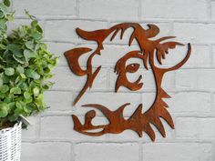 a metal cow head on a white brick wall next to a potted green plant