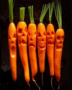 five carrots with faces carved into them are lined up in a row on a black surface