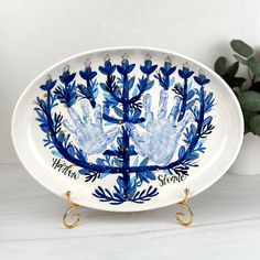 a blue and white platter with handprints on the bottom, in front of a potted plant