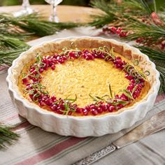 a pie with cranberries and green sprigs sits on a plaid tablecloth