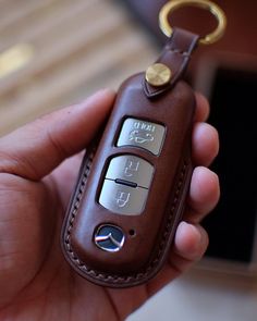 a hand holding a brown leather keychain that has two keys attached to it