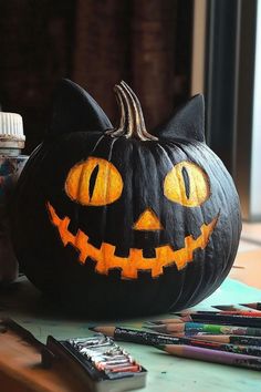 a black cat pumpkin with yellow eyes on a table next to some crayons