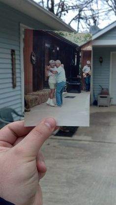 someone holding up an old photo in front of their house