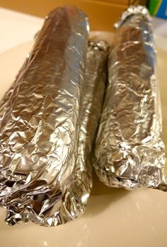 two foil wrapped burritos sitting on top of a counter