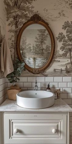 a white sink sitting under a mirror in a bathroom next to a wallpapered wall