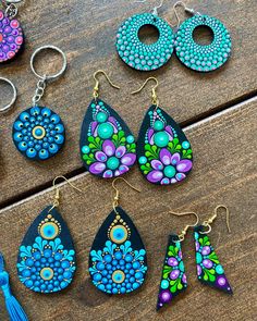 six pairs of earrings with different designs on them sitting on a wooden table next to some tassels